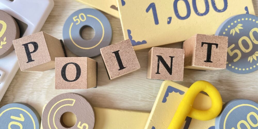 カラフルなコインや数字の書かれたボードゲームの部品が並び、中央に「POINT」と書かれた木製ブロックが置かれています。