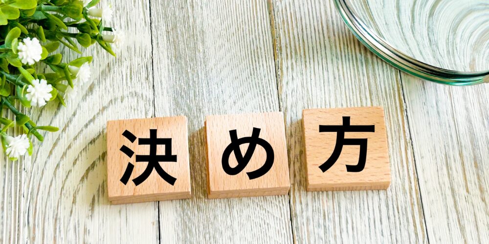 白木のテーブル上に緑の観葉植物が置かれ、その前に『決』『め』『方』と書かれた三つの木製ブロックが並んでいる様子