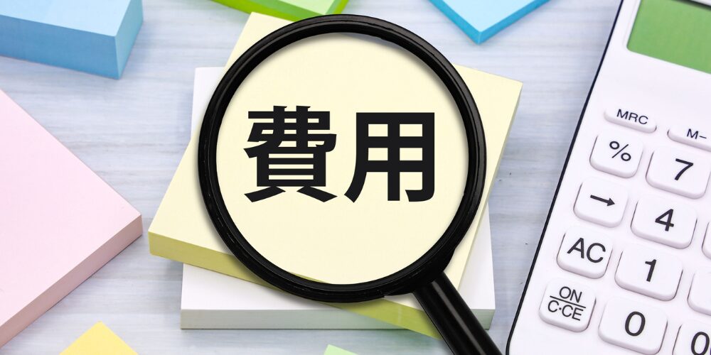 付箋に印刷された『費用』という文字を拡大するようにのせられたルーペと、そばに置かれた電卓やパステルカラーの付箋が写った一枚」