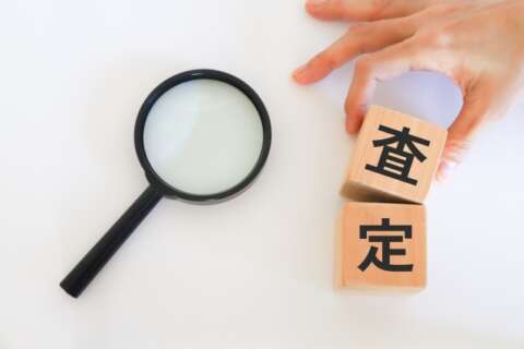 査定と書かれた木のブロックとそれを掴む手元。虫眼鏡