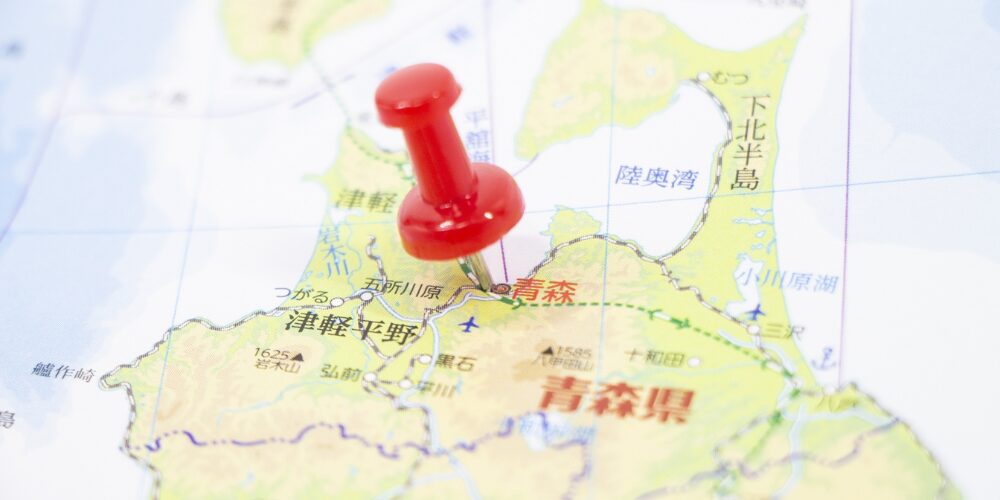 日本地図の上に赤い画鋲が刺さり、『青森県』の位置を示しているクローズアップ写真