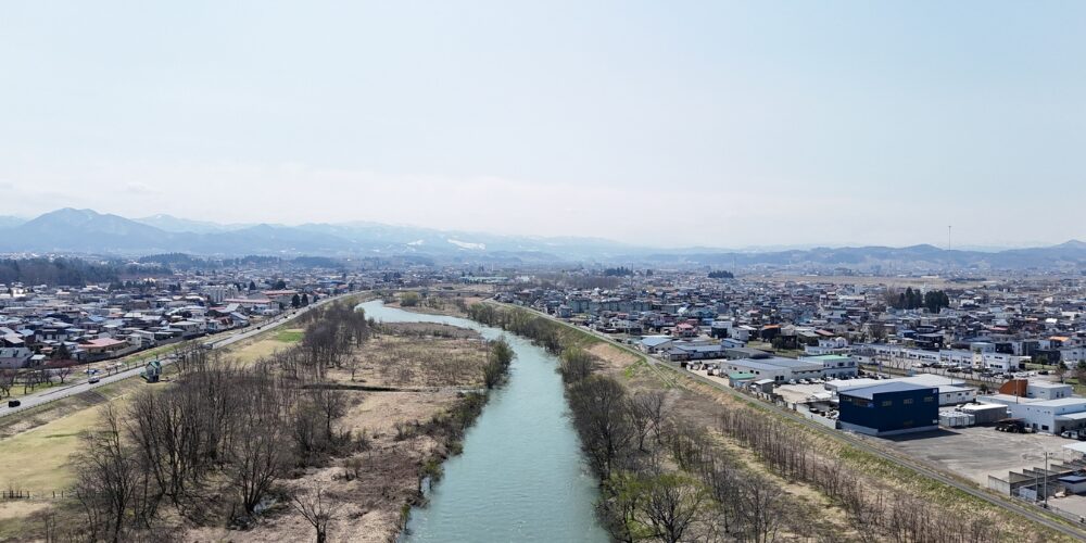 中央をゆったりと流れる川を軸に、左右に広がる市街地と、遠方の山並みが一望できる俯瞰風景