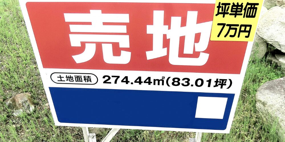 「売地」と大きく白抜き文字が入った赤い看板。右上に「坪単価7万円」、下部に「土地面積274.44㎡(83.01坪)」と記載。